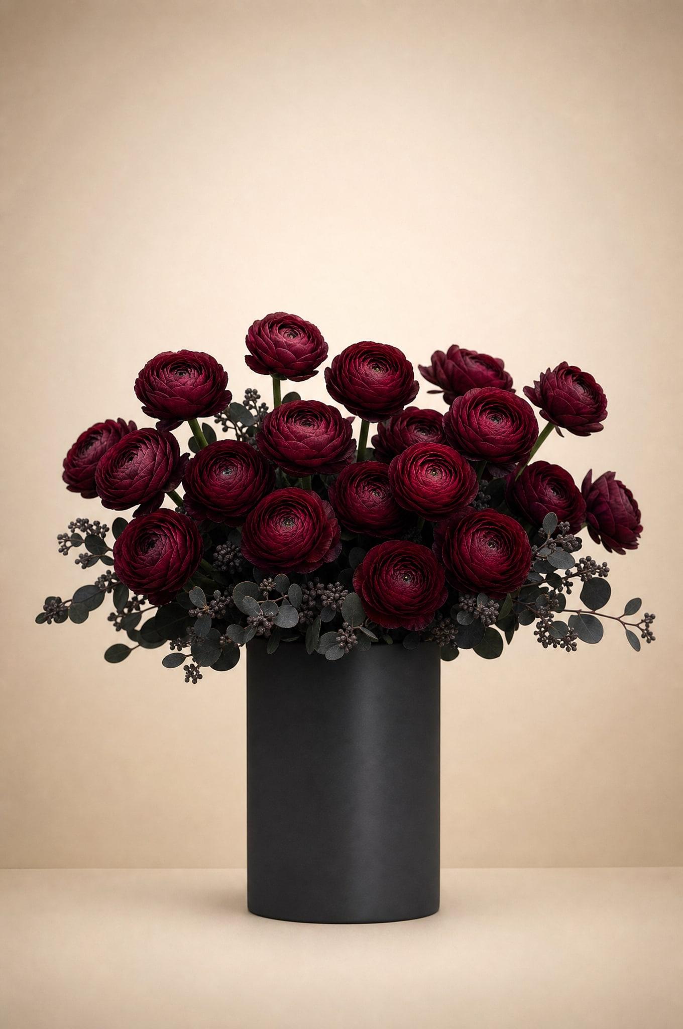 Deep burgundy ranunculus with dark seeded eucalyptus in a black cylinder vase