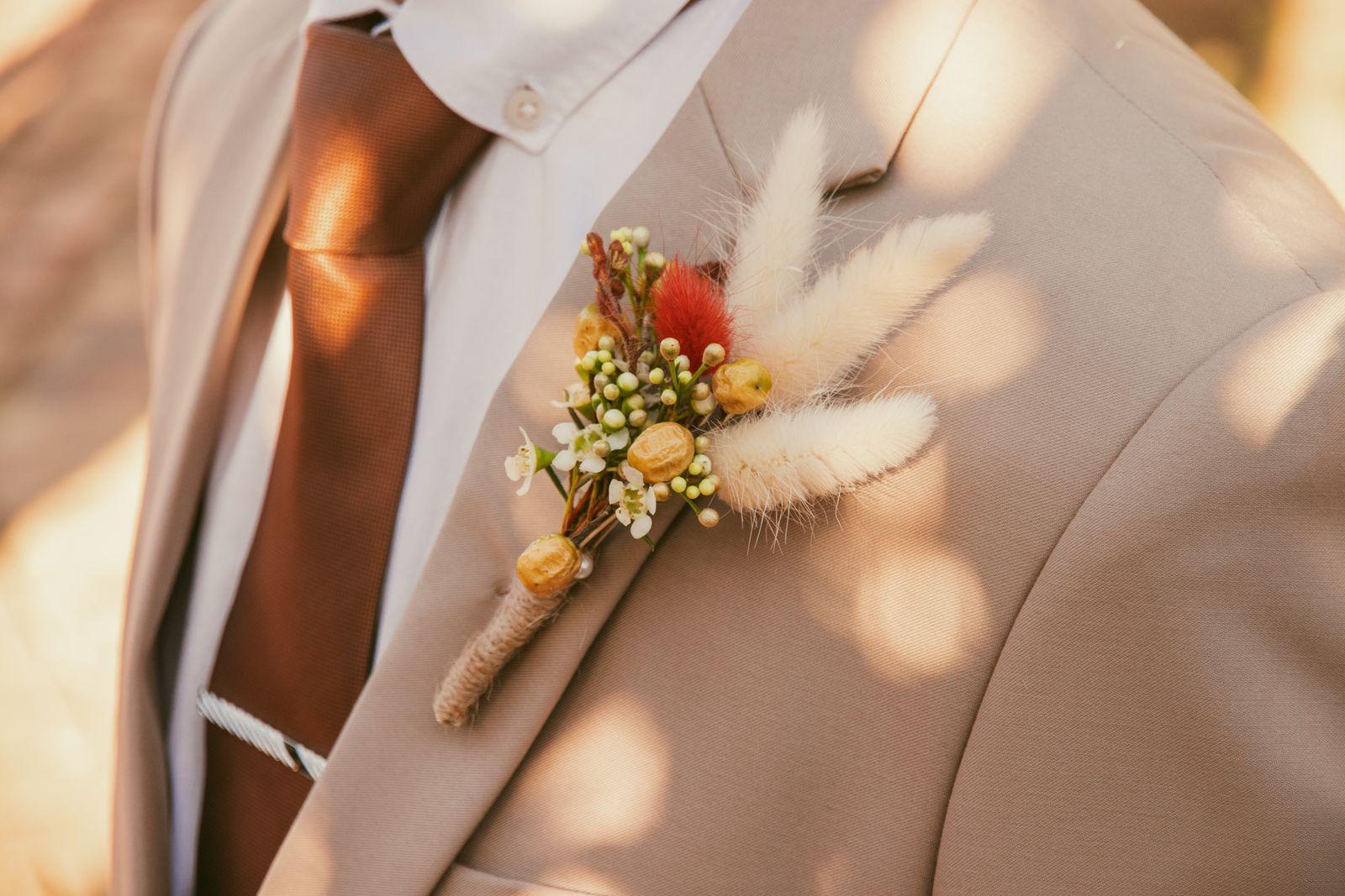 A wedding boutonniere pinned to the lapel of a tan suit