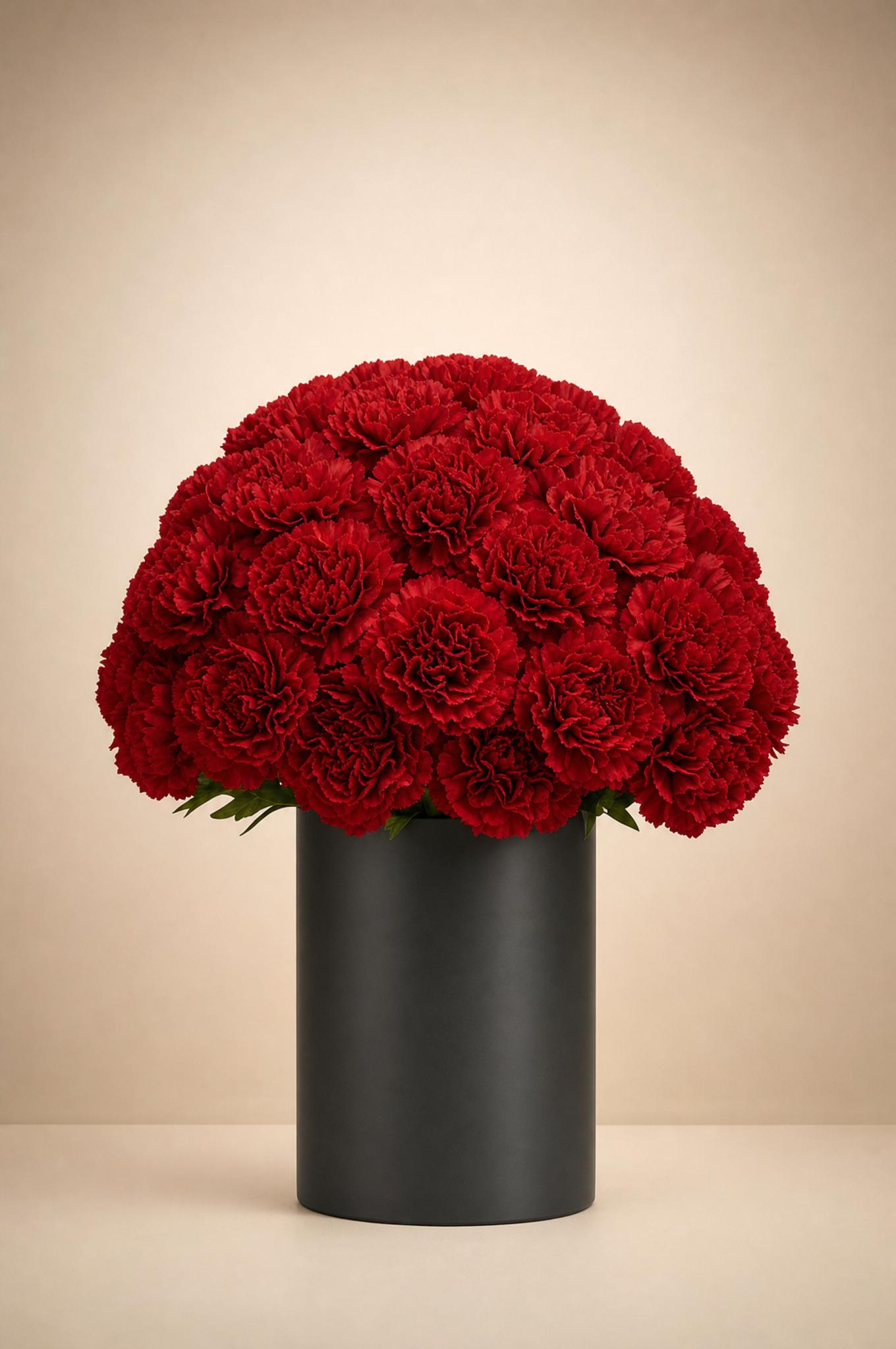 Rounded bouquet of deep crimson-red carnations in a matte charcoal cylinder vase
