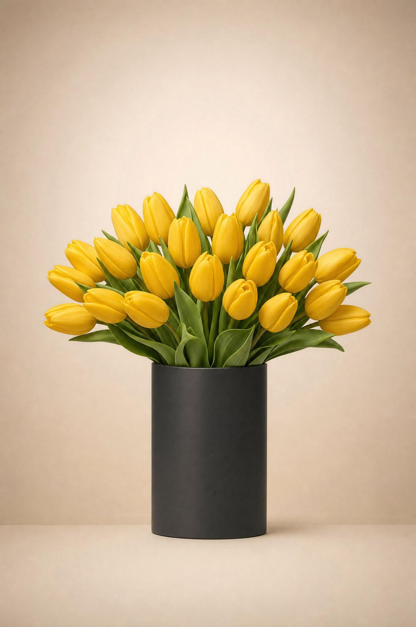 Bright golden-yellow tulips with green leaves in a black cylinder vase