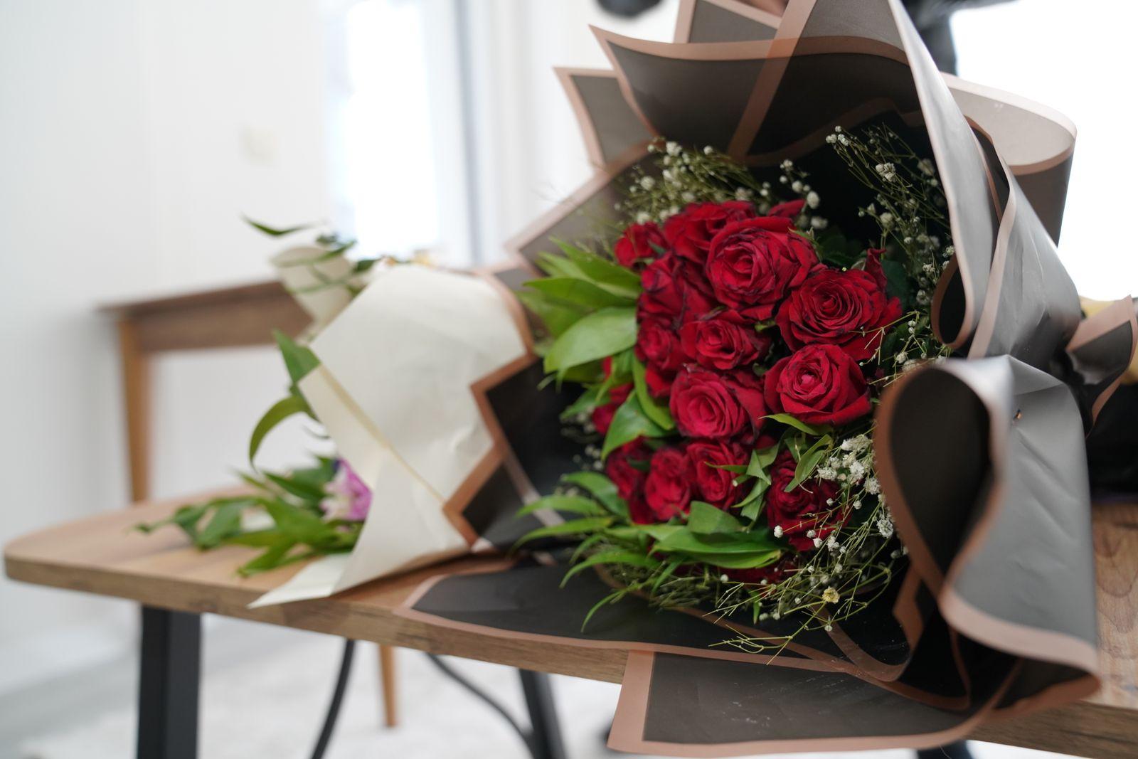 Red roses with baby's breath and greenery in black kraft-paper wrapping on a wooden bench