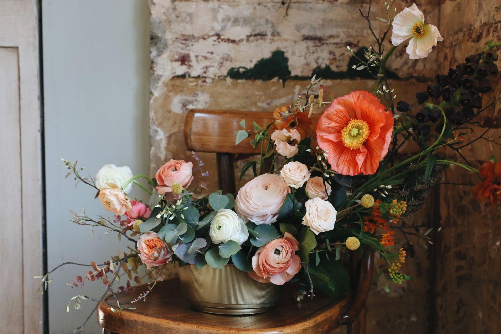 Autumnal arrangement of coral poppies, peach ranunculus and roses in a gold footed bowl