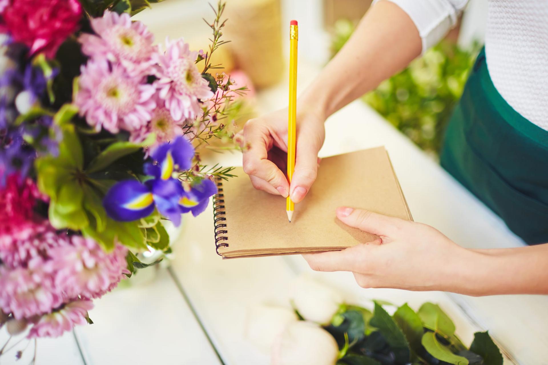 A florist working out prices with a notepad and pencil at the shop counter