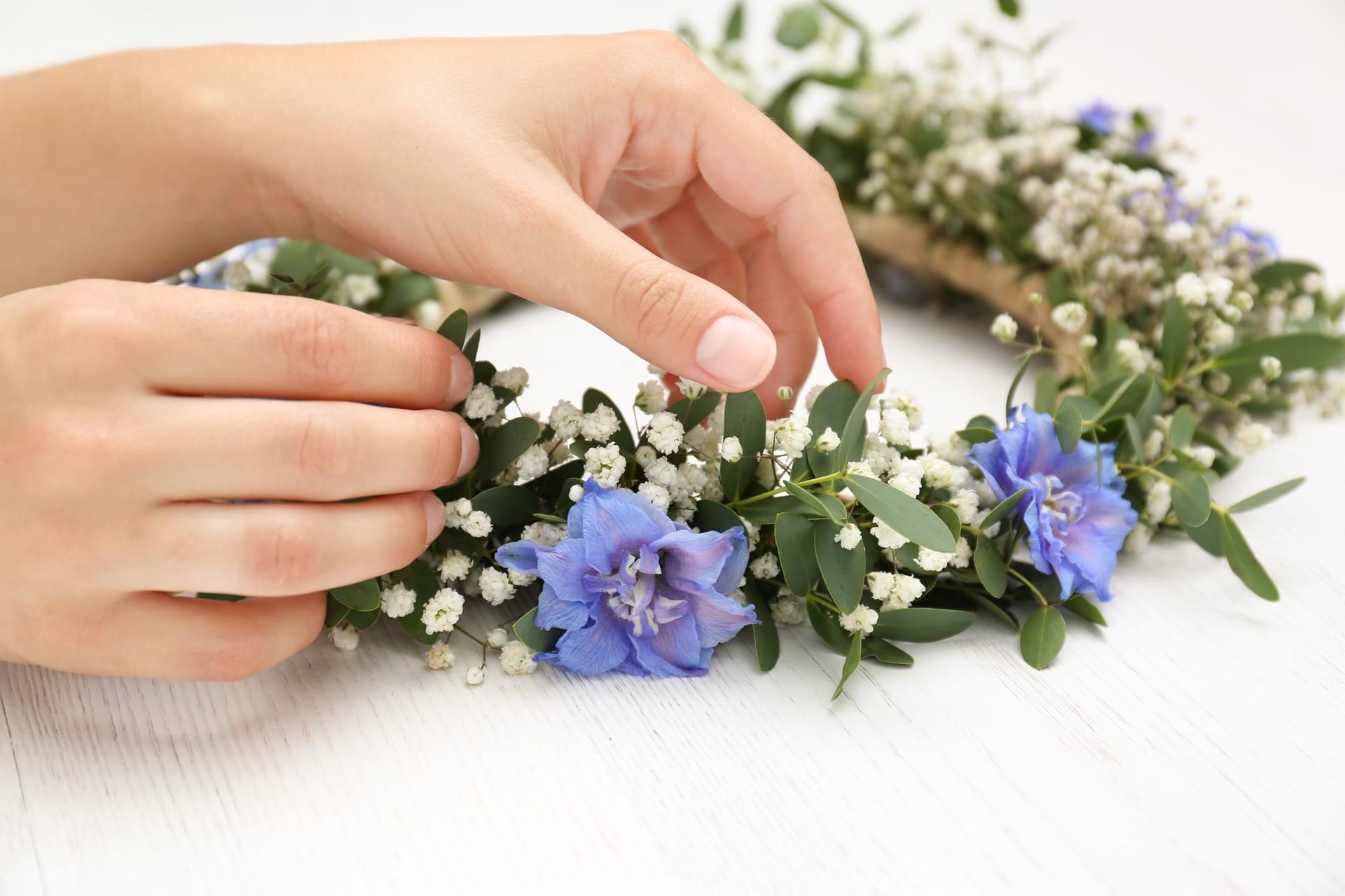 Hands weaving a flower crown at a wooden table