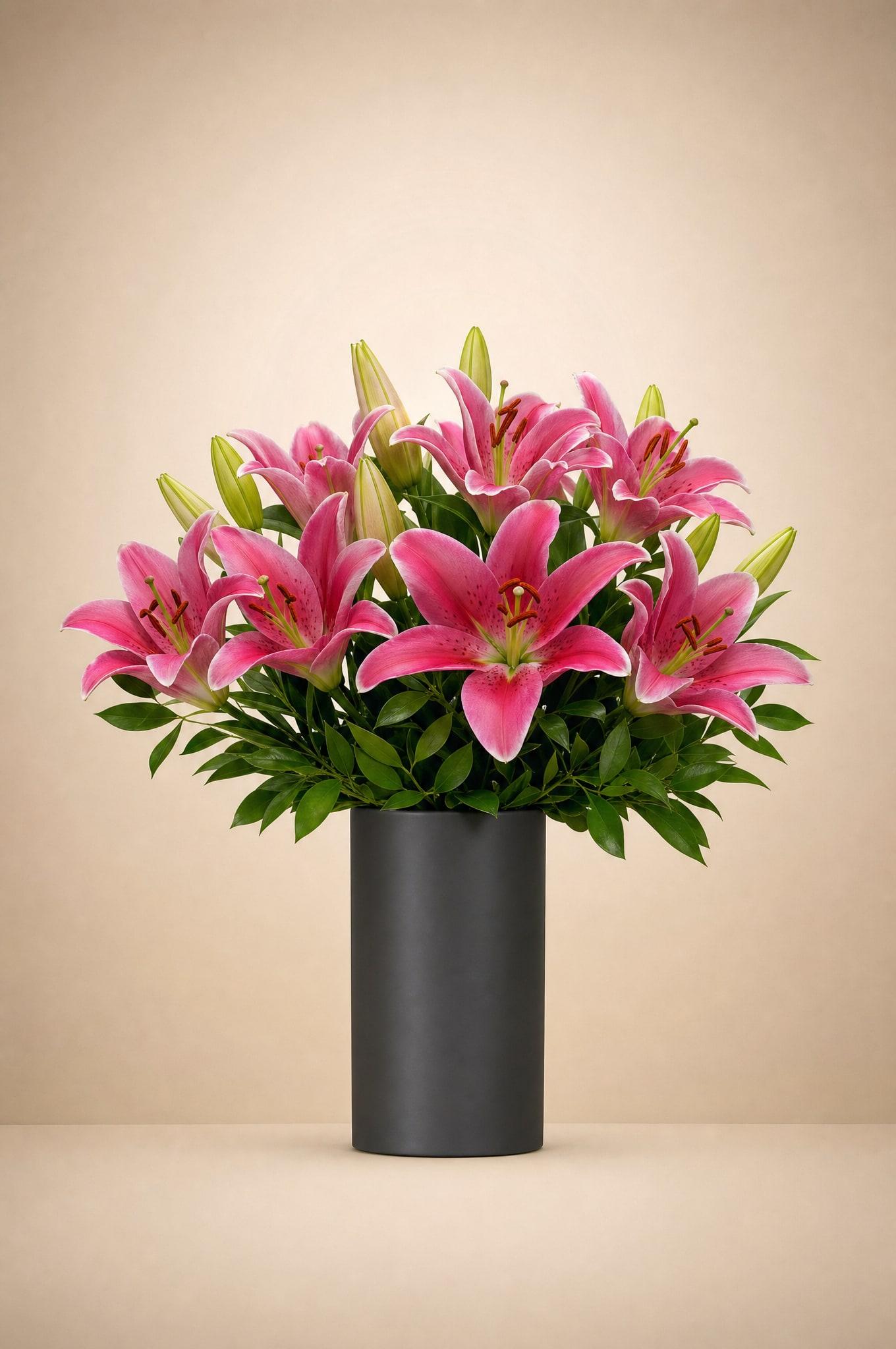 Vivid pink lilies with buds and glossy green foliage in a black cylinder vase