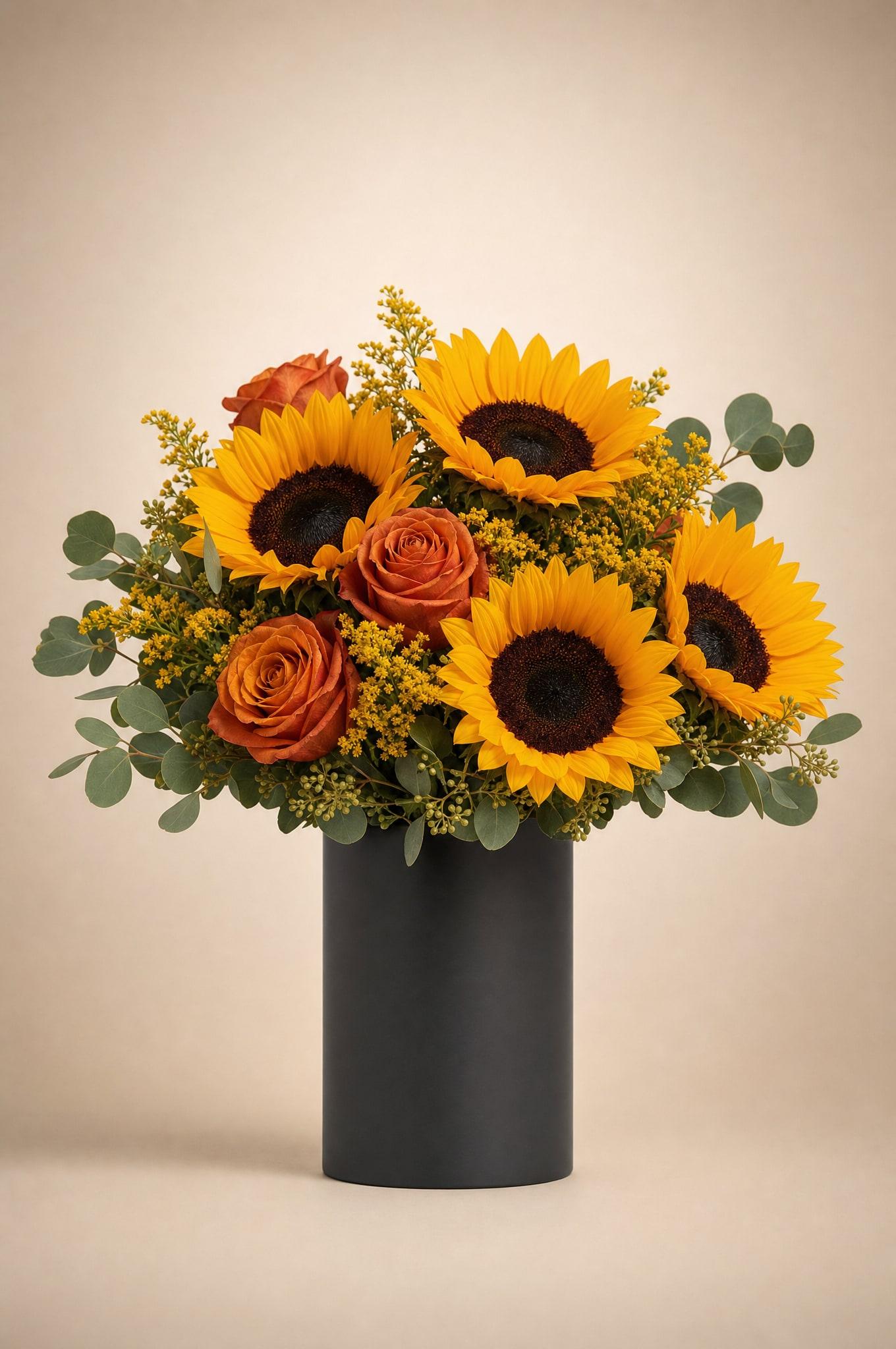 Sunflowers with burnt-orange roses, yellow solidago and eucalyptus in a matte black cylinder vase