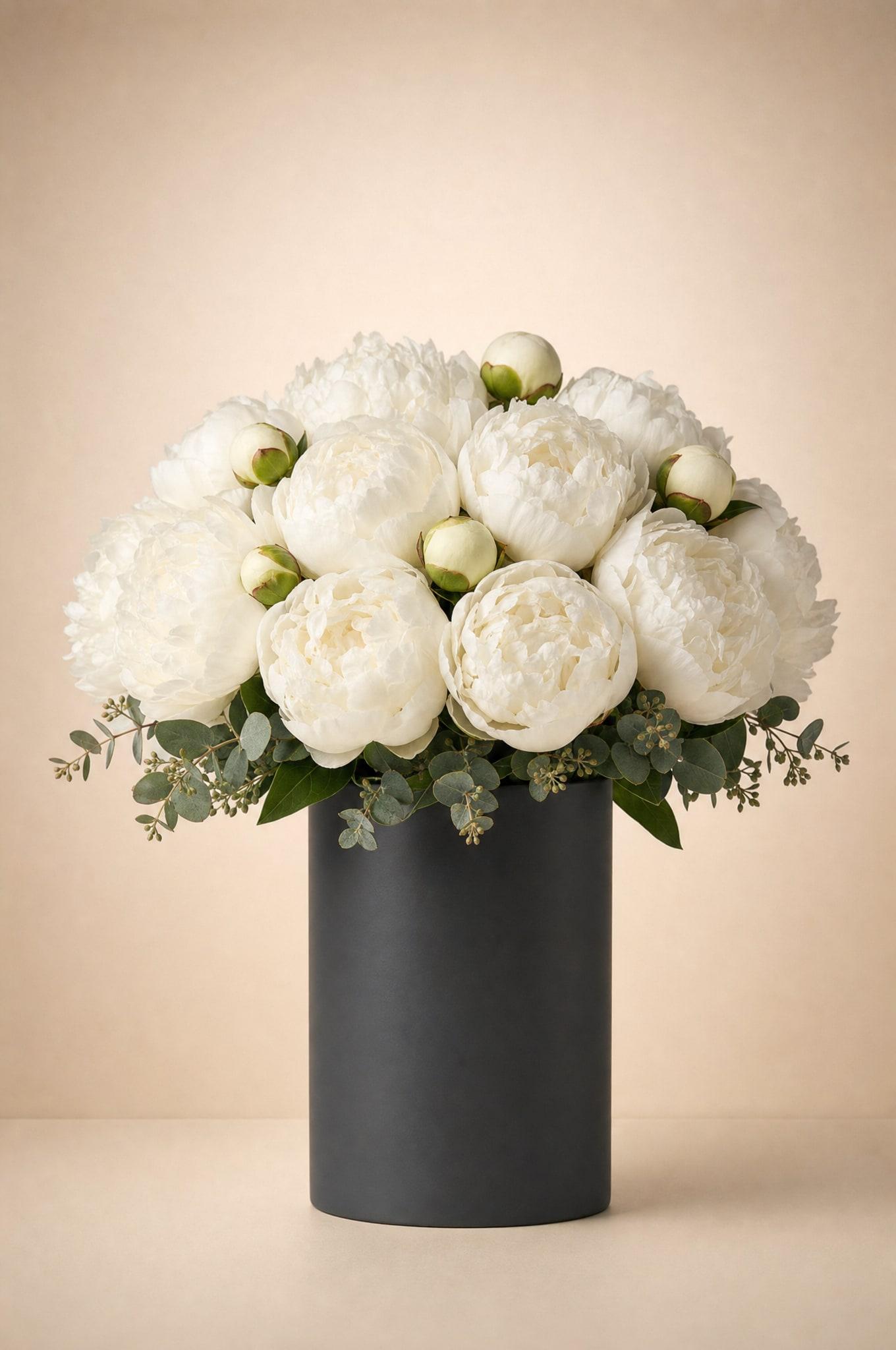 White peonies with green buds and seeded eucalyptus in a matte charcoal cylinder vase